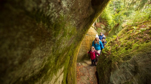 A family following a rugged trails between the high-sided rocks at Cragside, Northumberland.